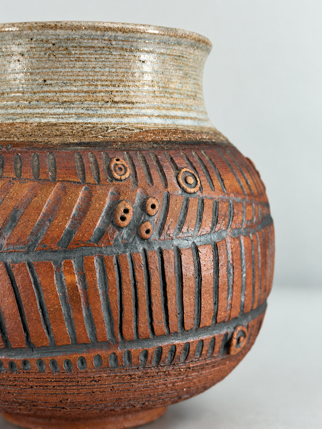 Close-up of an incised studio pottery vessel with cut lines, pressed clay forms and glaze pooling in the recesses