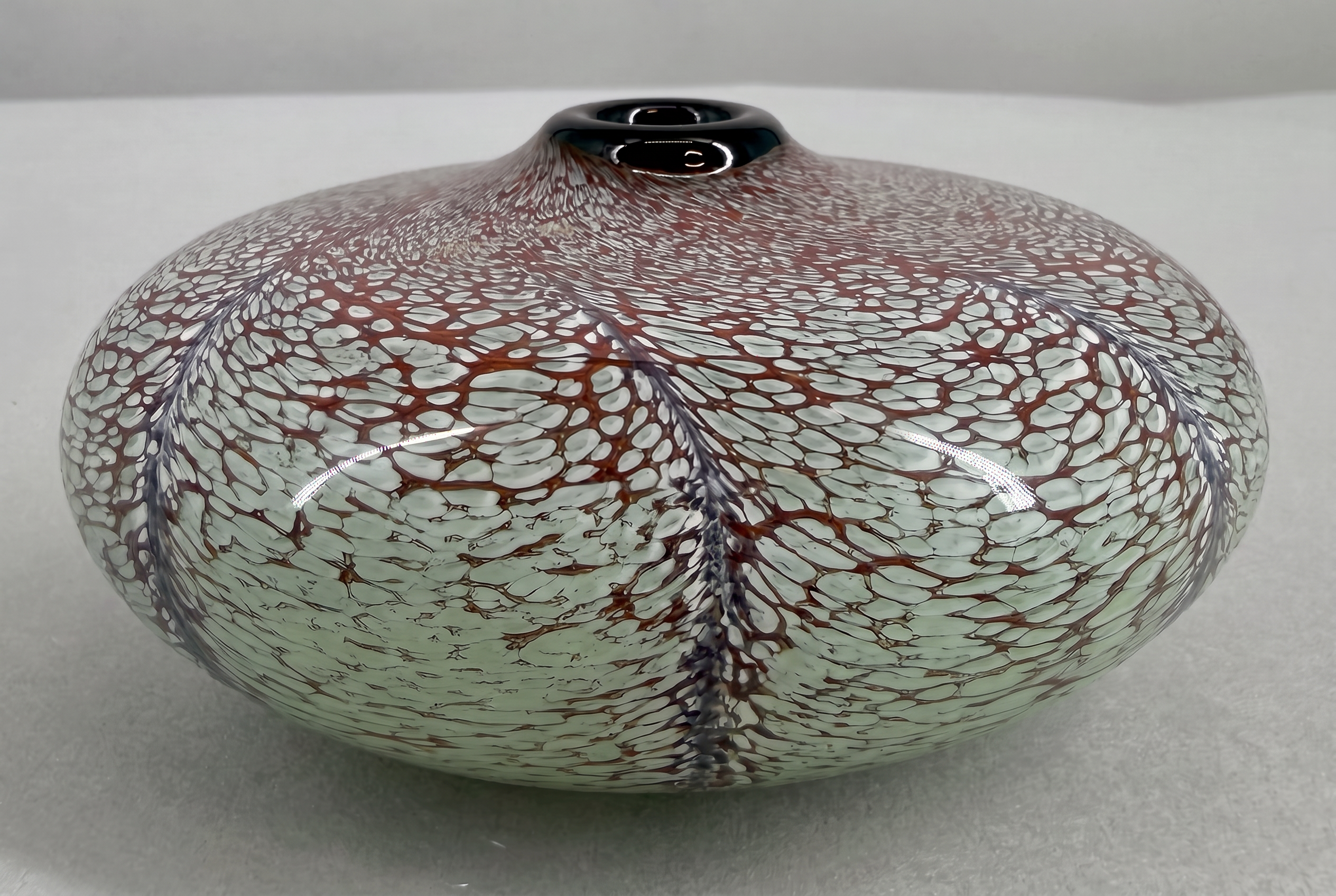 Hand-blown squat art-glass vessel with red and white lattice over pale green